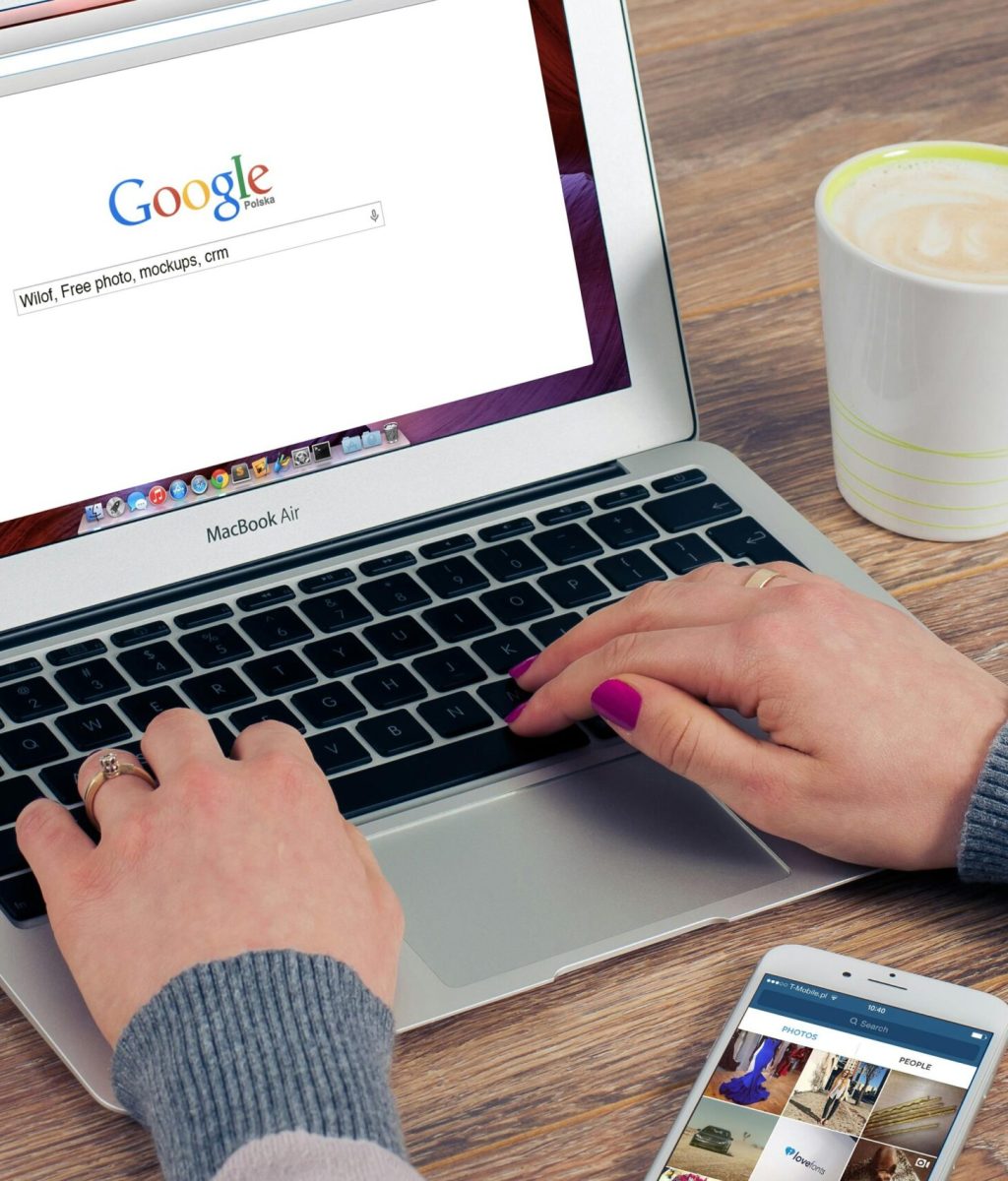 Hands typing on MacBook Air with Google search open, coffee nearby.