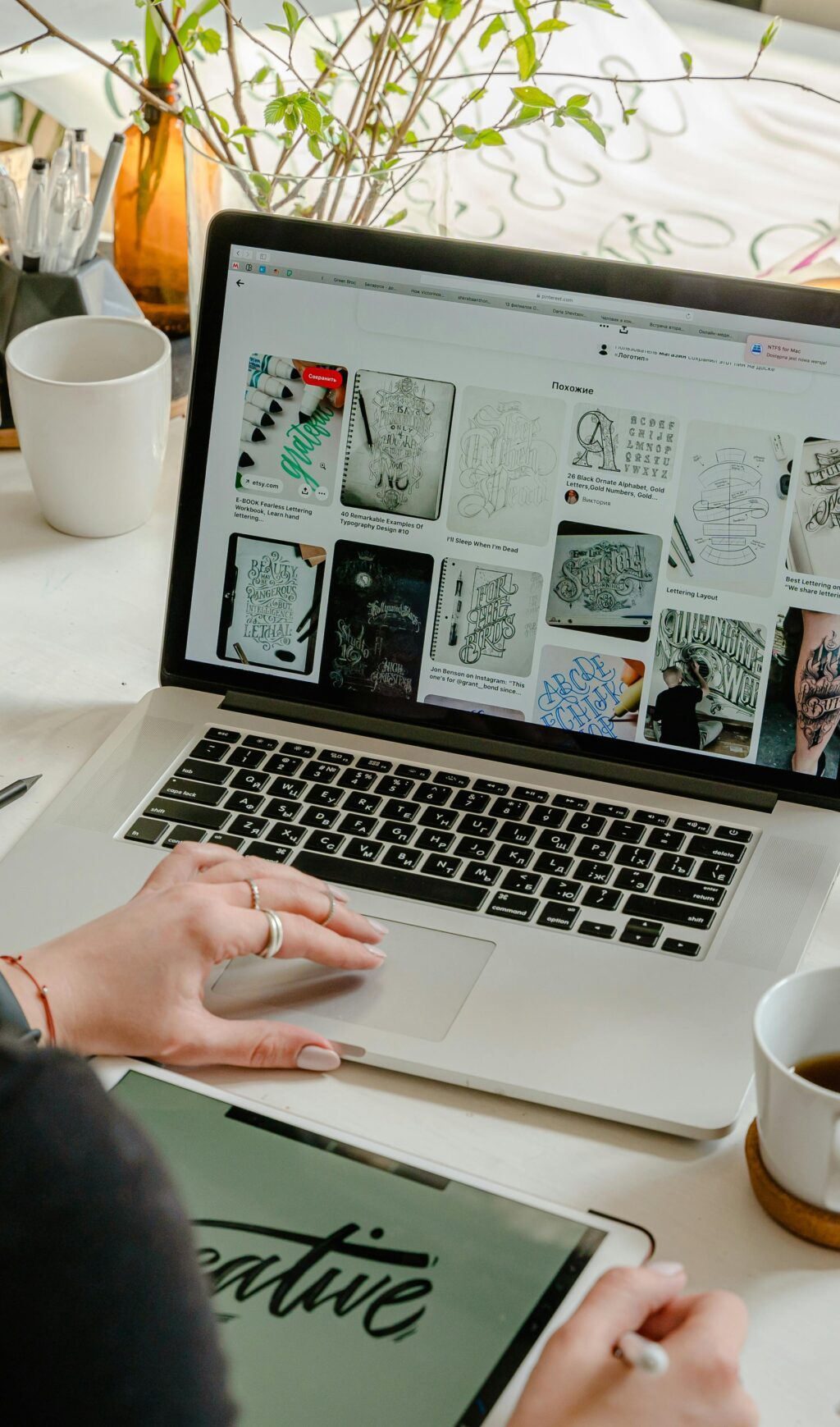 Woman in a creative workspace using a laptop and tablet for calligraphy. Artistic and tech-driven environment.